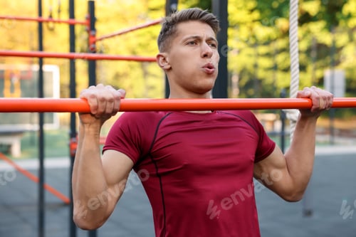 Preview: Athletic young man doing pull ups at outdoor gym