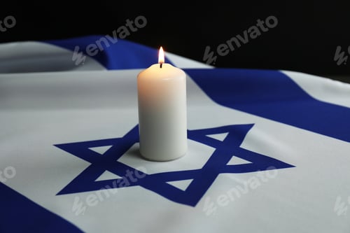 Preview: Holocaust Remembrance Day. Burning candle on flag of Israel against dark background, closeup