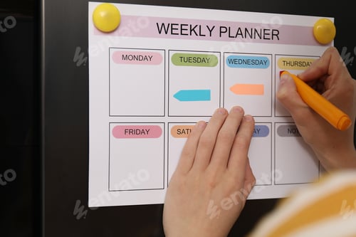 Preview: Woman using weekly planner on refrigerator indoors, closeup