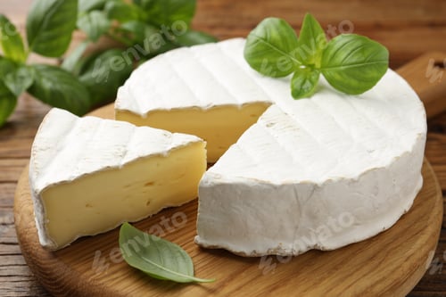 Preview: Cut delicious brie cheese and basil on wooden table, closeup