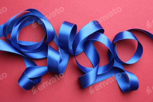 Preview: Beautiful blue ribbon on red background, top view