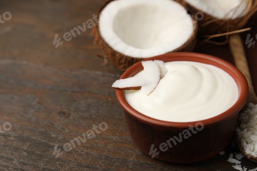 Preview: Delicious coconut yogurt in bowl, flakes and halves of fruit on wooden table, closeup. Space for tex