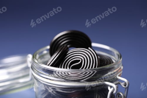 Preview: Natural licorice candies in glass jar on dark blue background, closeup