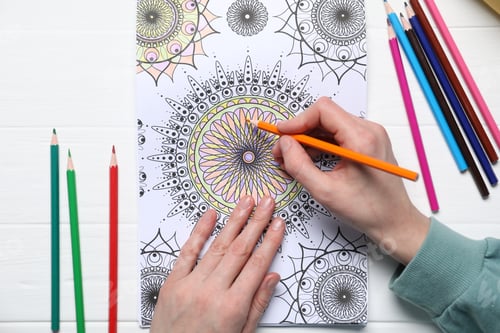 Preview: Woman coloring antistress picture with pencils at white table, top view