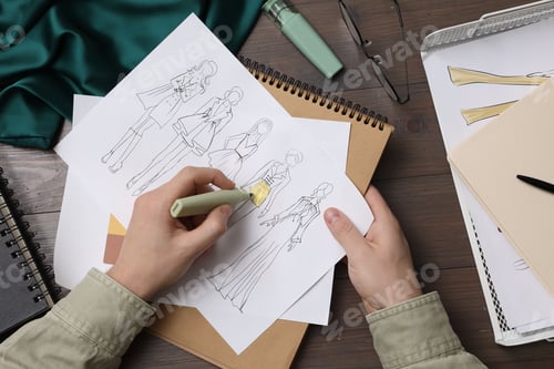 Preview: Fashion designer drawing sketch of outfits at wooden desk, closeup