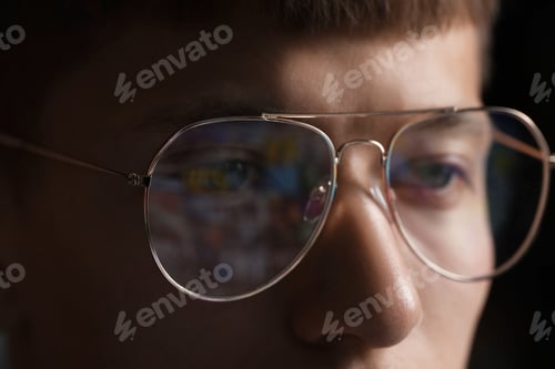 Preview: Young man wearing glasses with reflection on dark background, closeup