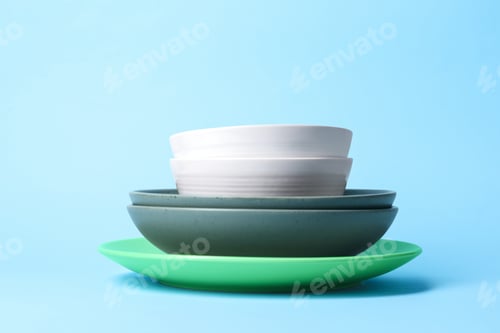 Preview: Stack of clean dishes on light blue background, closeup