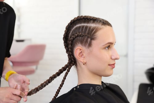 Preview: Hairstylist braiding teenage girl's hair in salon, closeup