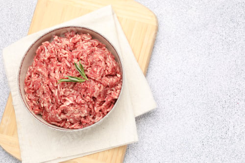 Preview: Raw minced beef meat with rosemary on light grey table, top view. Space for text