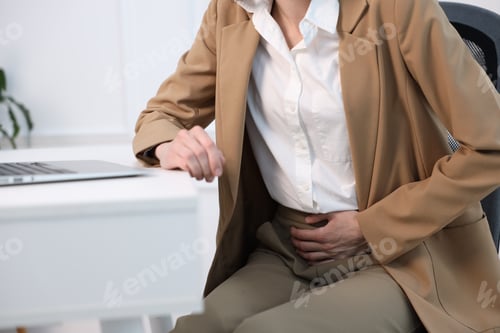 Preview: Woman in suit suffering from menstrual pain at workplace, closeup