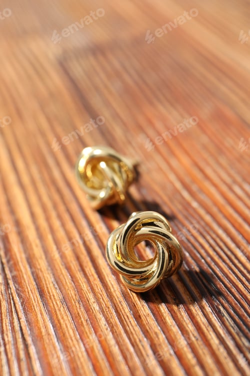 Preview: Pair of golden earrings on wooden table, closeup