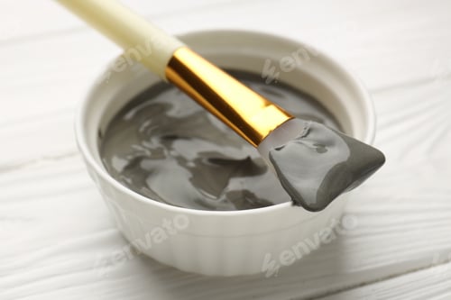 Preview: Mud therapy. Natural clay paste for facial and body care and brush on white wooden table, closeup