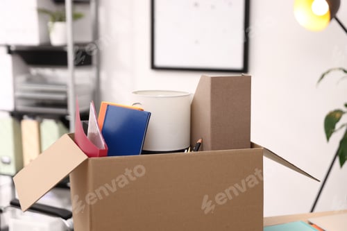 Preview: Dismissal. Different personal belongings in cardboard box on table in office, closeup
