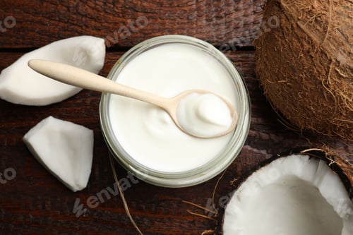 Preview: Tasty coconut yogurt in jar, spoon and fruits on wooden table, flat lay