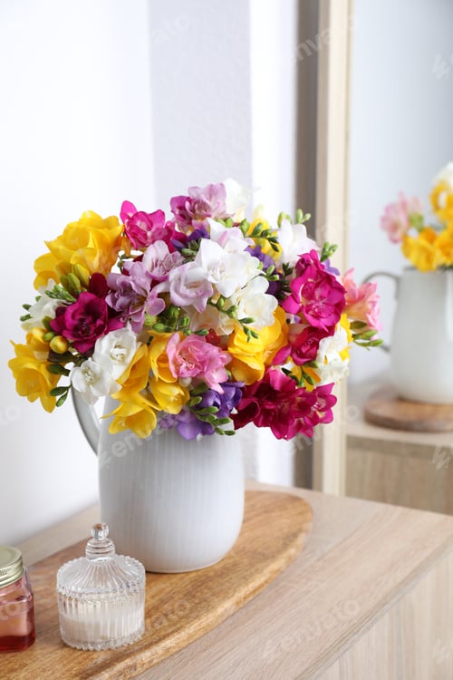 Preview: Beautiful freesia flowers in vase and candles on wooden table near white wall indoors, closeup