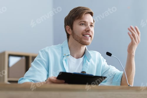 Preview: Speaker with microphone performing at desk indoors, low angle view