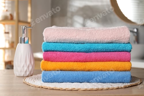 Preview: Stack of colorful towels and soap on wooden table in bathroom, closeup