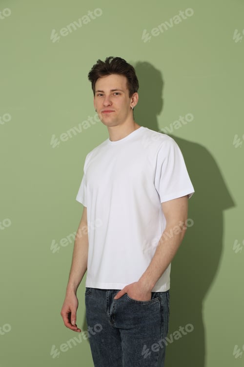 Preview: Handsome young man wearing blank white t-shirt on light green background. Mockup for design
