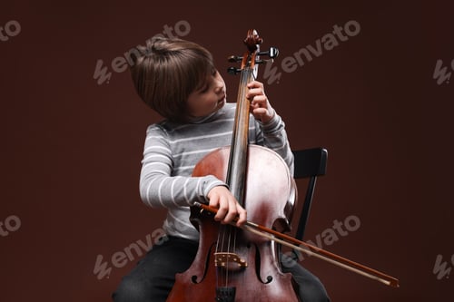 Preview: Cute little boy playing violoncello on brown background