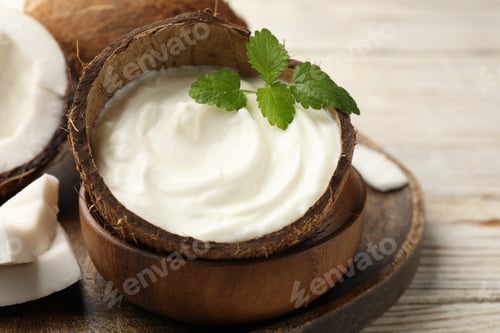 Preview: Tasty coconut yogurt with melissa leaves in shell and nuts on white wooden table, closeup