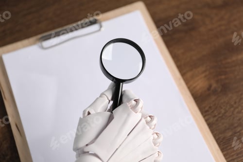 Preview: Mannequin hand with magnifying glass and clipboard on table, above view