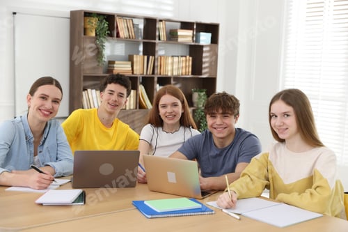 Preview: Group of students studying with laptops and notebooks at wooden desk in classroom