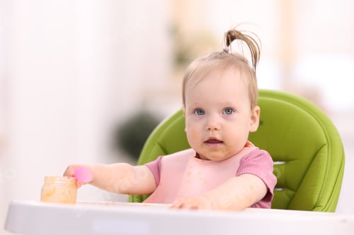 Preview: Cute little child eating baby food on feeding chair at home