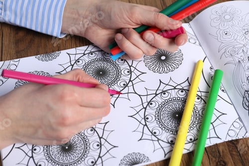 Preview: Woman coloring antistress picture with felt tip pen at wooden table, closeup