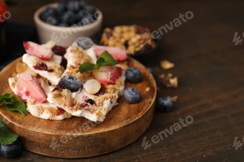Preview: Pieces of tasty yogurt bark with berries, mint and granola on wooden table, closeup. Space for text
