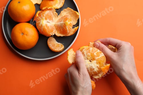 Preview: Woman peeling ripe tangerine and fresh fruits on orange background, top view