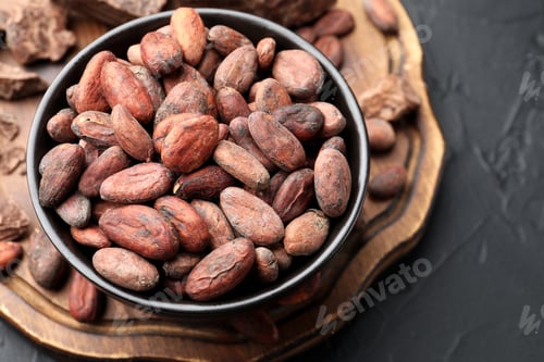 Preview: Fresh cocoa beans in bowl on dark textured table, above view. Space for text