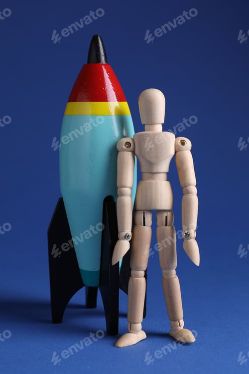 Preview: Wooden mannequin with toy rocket on blue background, closeup