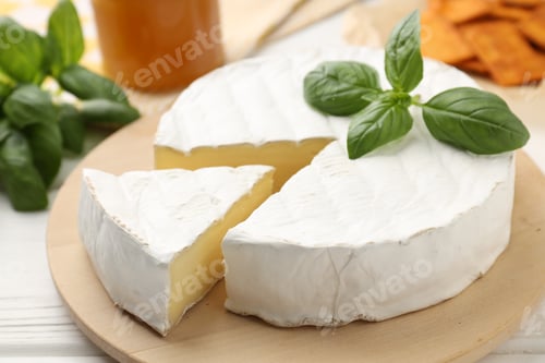 Preview: Cut delicious brie cheese and basil on white wooden table, closeup