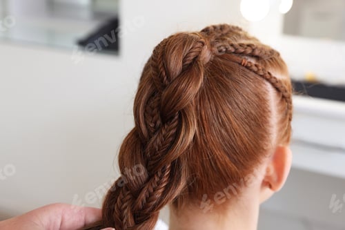 Preview: Hairstylist braiding teenage girl's hair in salon, closeup