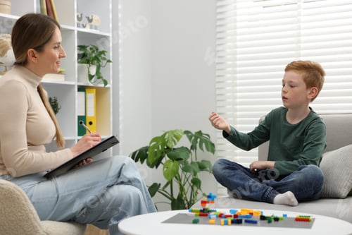 Preview: Professional child psychologist working with boy on sofa indoors