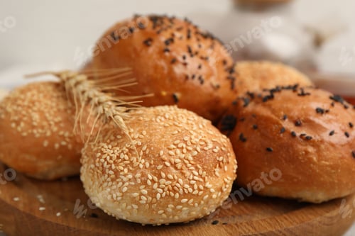 Preview: Yummy buns with sesame seeds and wheat ear on table, closeup