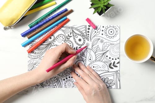 Preview: Woman coloring antistress picture with felt tip pen at white table, top view