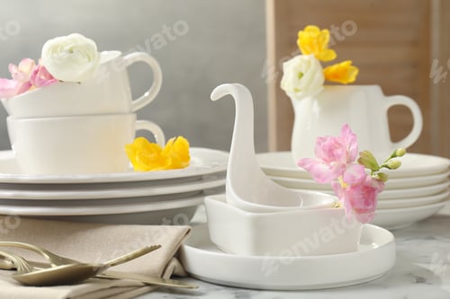 Preview: Many clean dishware, cutlery and beautiful flowers on white marble table indoors, closeup