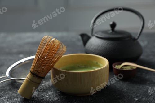 Preview: Refreshing green matcha in ceramic bowl, bamboo whisk, powder, scoop, teapot and sifter on black tex