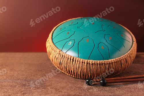 Preview: Steel tongue drum and mallets on grey textured table against brown background, closeup. Space for te