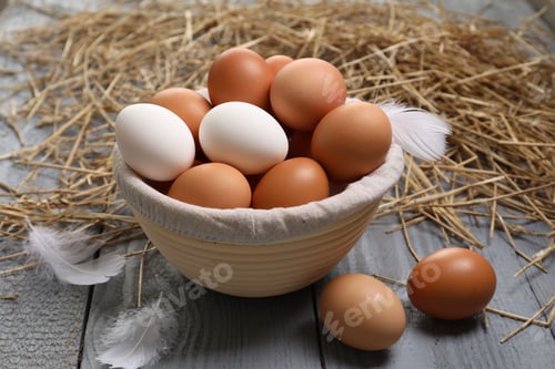 Preview: Fresh chicken eggs in bowl, feathers and dried straw on grey wooden table