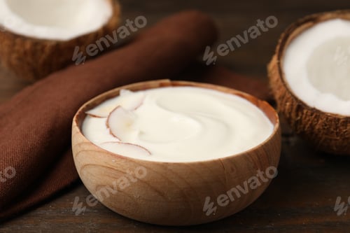 Preview: Delicious coconut yogurt with flakes in bowl and halves of fruit on wooden table, closeup