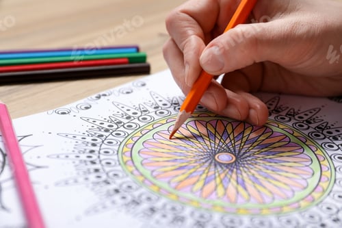 Preview: Woman coloring antistress picture with pencils at wooden table, closeup