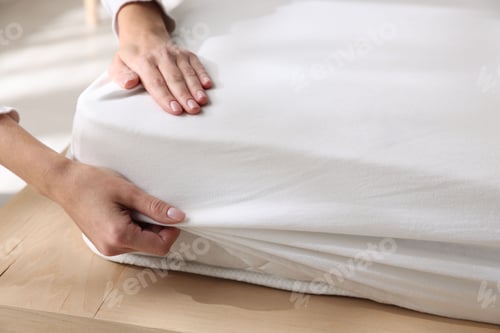 Preview: Woman putting bed sheet on mattress indoors, closeup