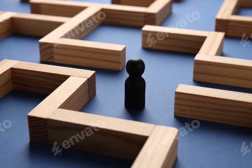 Preview: Maze made of wooden blocks and human figure on blue background, closeup. Business strategy