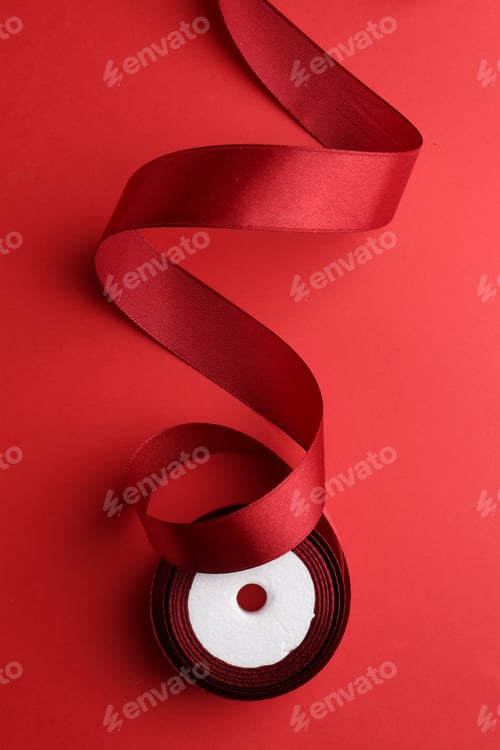 Preview: Roll of red ribbon on color background, top view