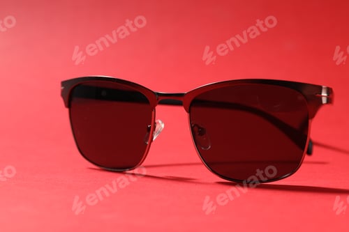 Preview: Pair of stylish sunglasses on red background, closeup