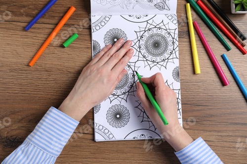 Preview: Woman coloring antistress picture with felt tip pen at wooden table, top view