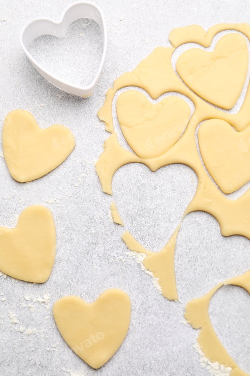 Preview: Uncooked heart shaped cookies, raw dough and cookie cutter on light gray table, flat lay