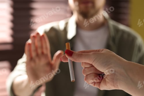 Preview: Man refusing cigarette from woman indoors, selective focus. Smoking cessation